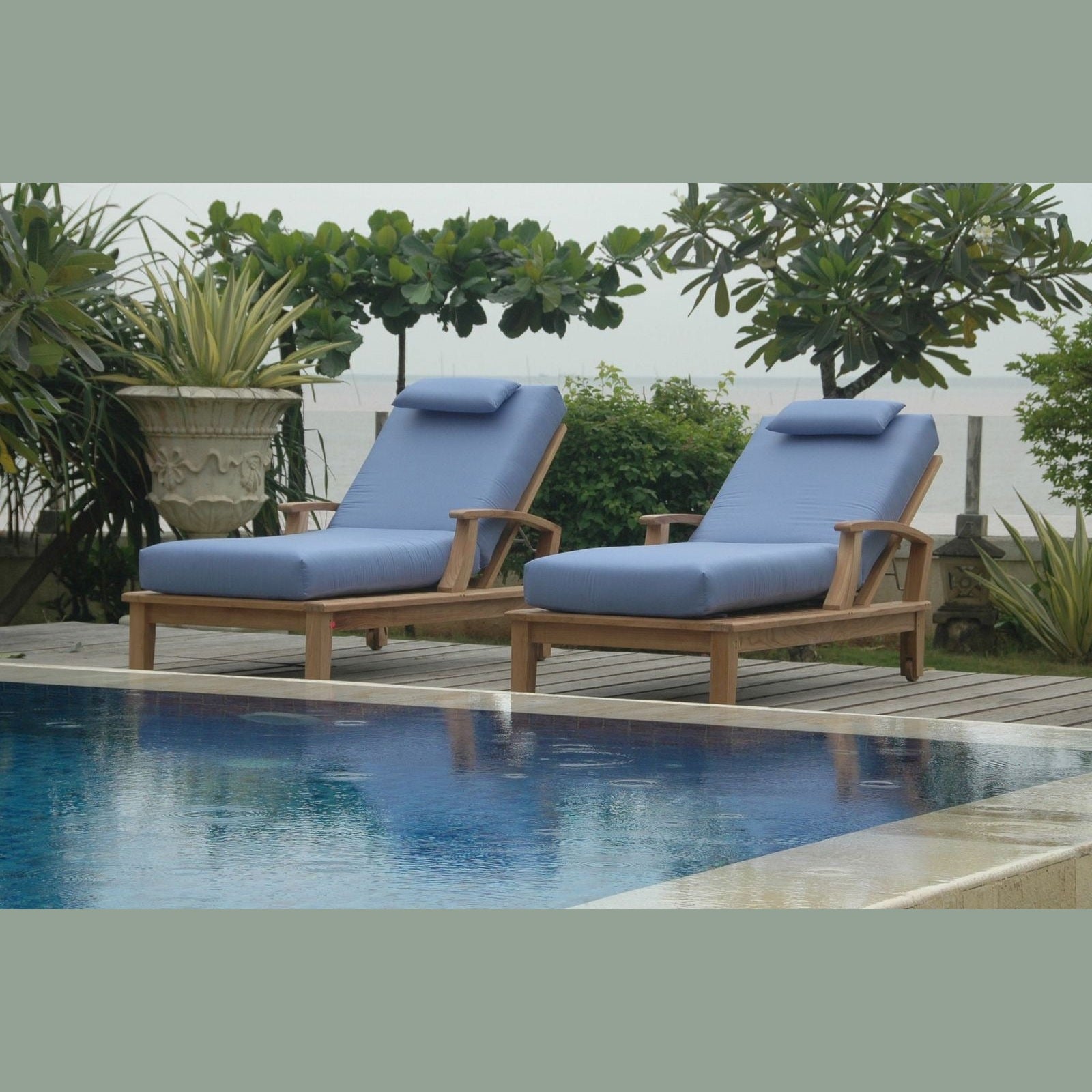 Two blue cushioned lounge chairs by a pool with greenery in the background