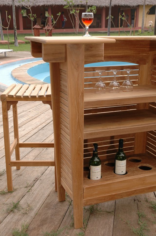 Wooden outdoor bar with wine bottles and glasses near a pool