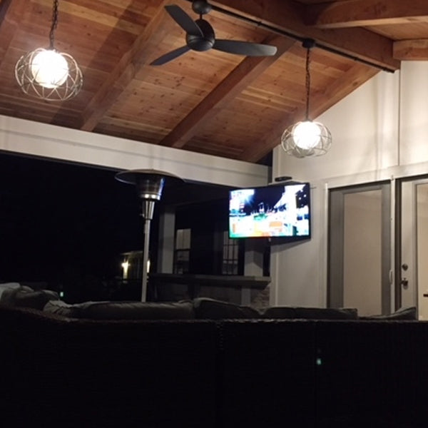 Outdoor living area with a TV screen displaying a sports event, surrounded by wooden beams and ceiling lights.