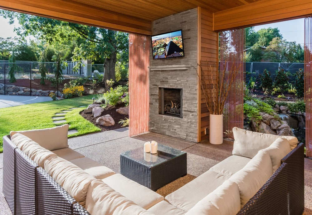 Outdoor living space with patio furniture, fireplace, and television screen.