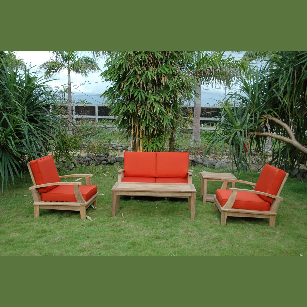 Outdoor furniture set with red cushions on a grassy area with trees in the background