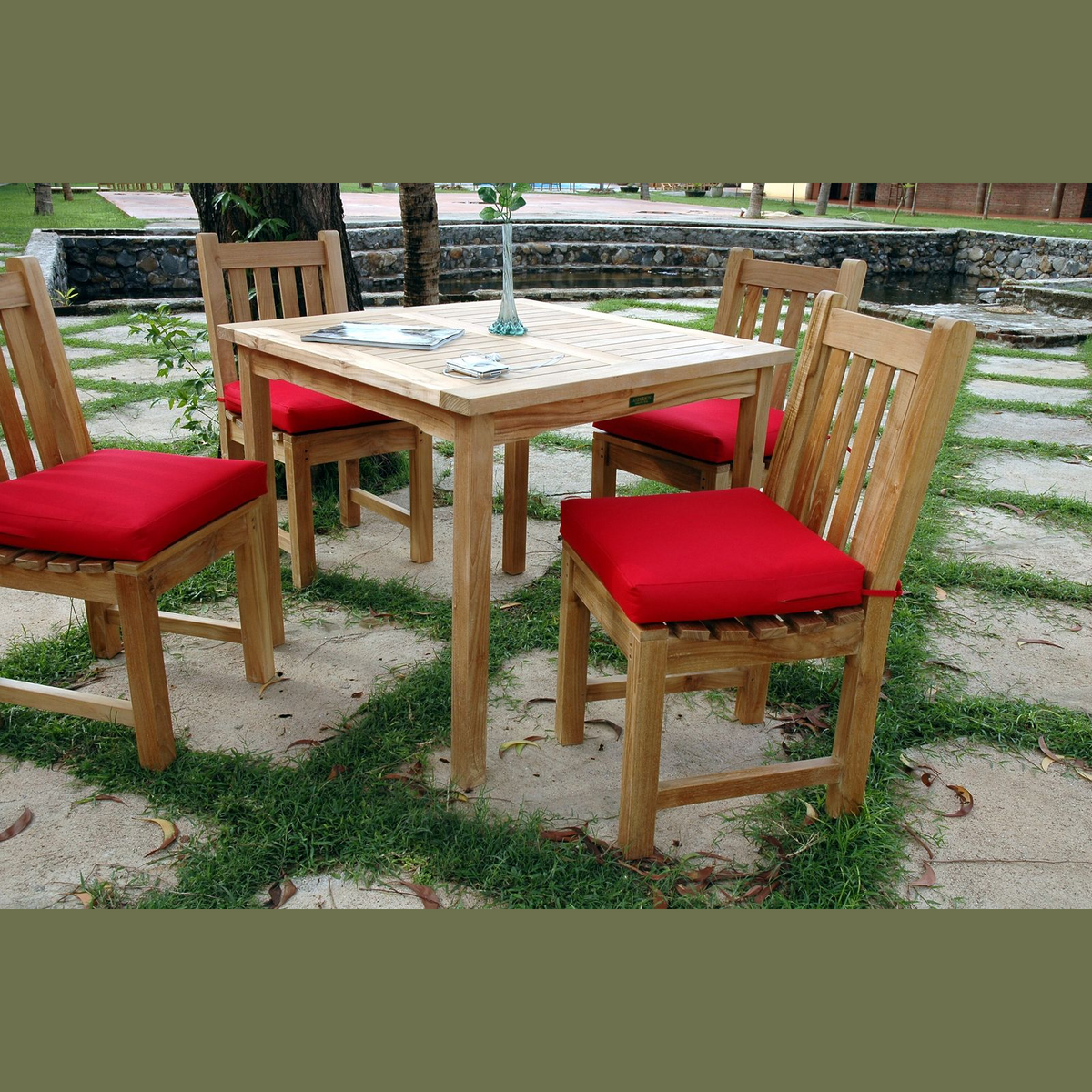 Wooden outdoor table with four matching chairs and red cushions, set on a stone patio.