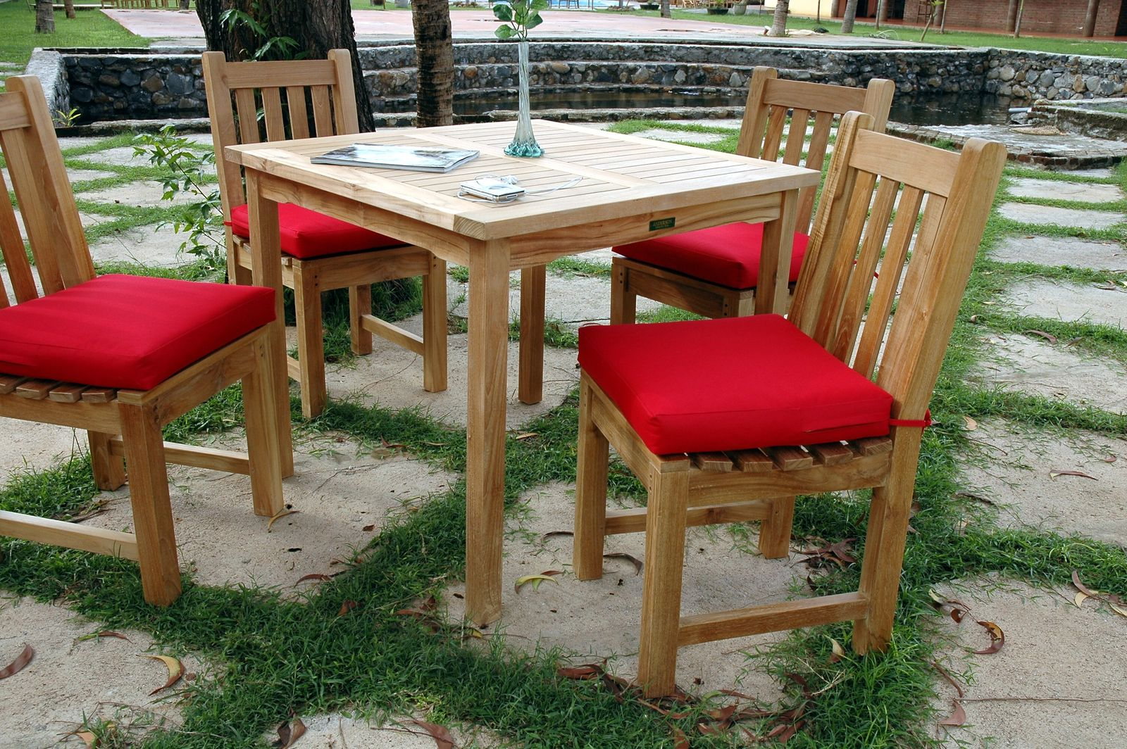 Wooden outdoor table with four matching chairs and red cushions, set on a stone patio.