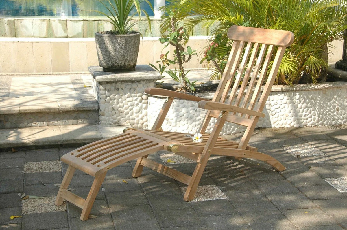 Wooden lounge chair with ottoman on a patio with plants and steps in the background