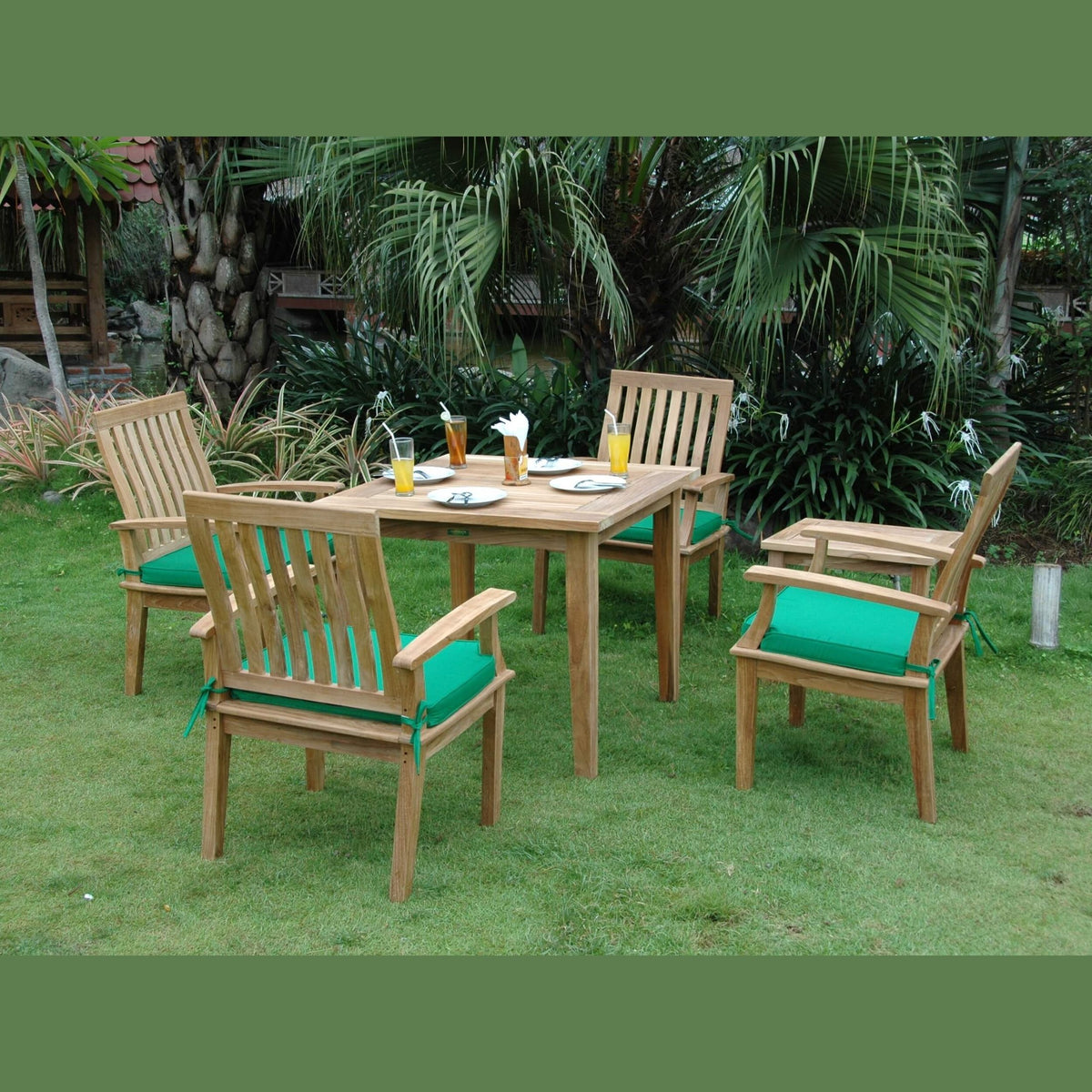 Outdoor dining set with wooden chairs and table on a grassy area with green cushions.