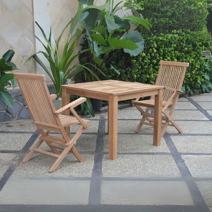 Wooden outdoor table with two chairs on a stone patio surrounded by plants