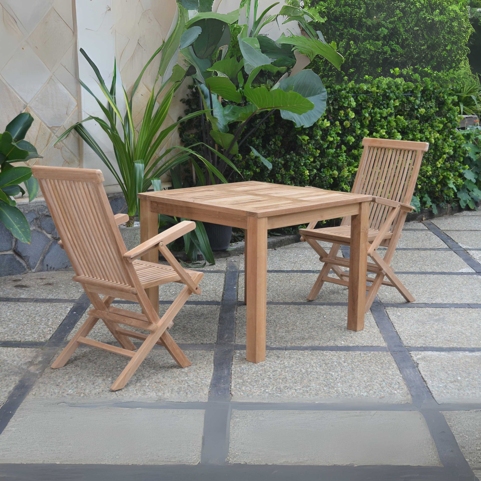 Wooden outdoor table with two chairs on a stone patio surrounded by plants