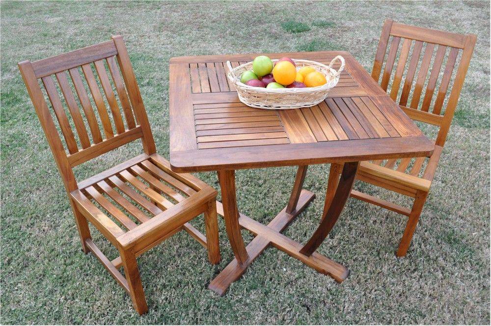 Wooden outdoor table with two chairs and a basket of fruit on a grassy background