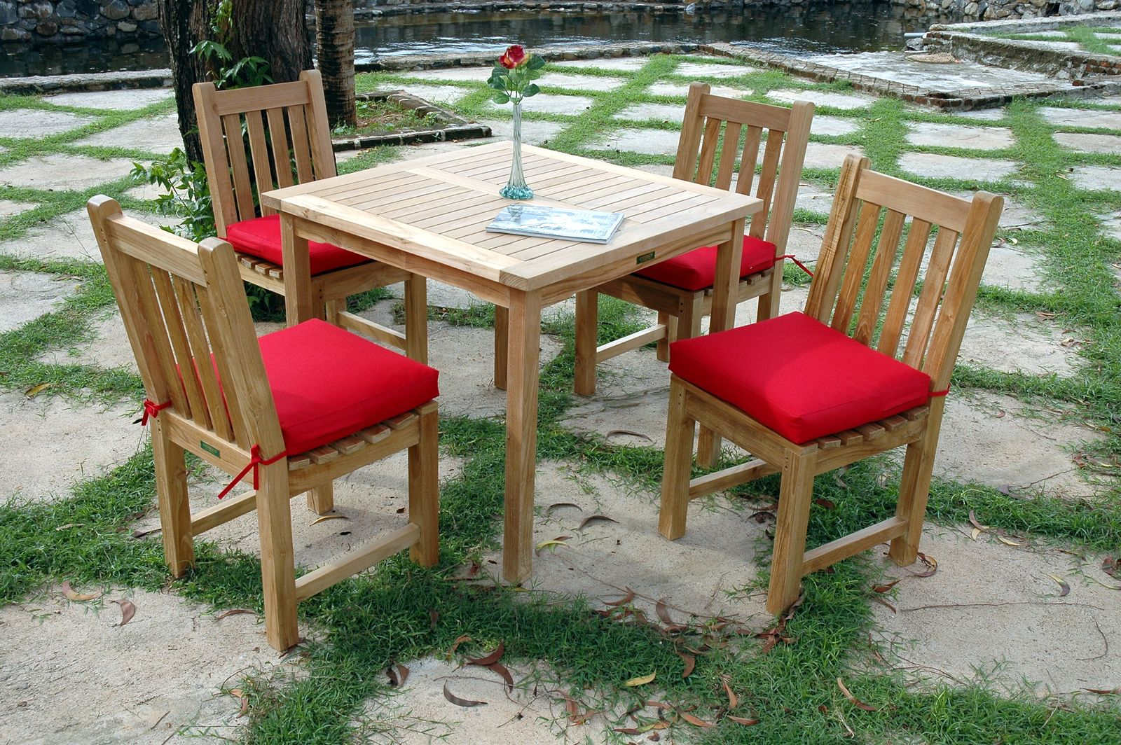 Wooden outdoor table set with four chairs and red cushions on a stone patio.