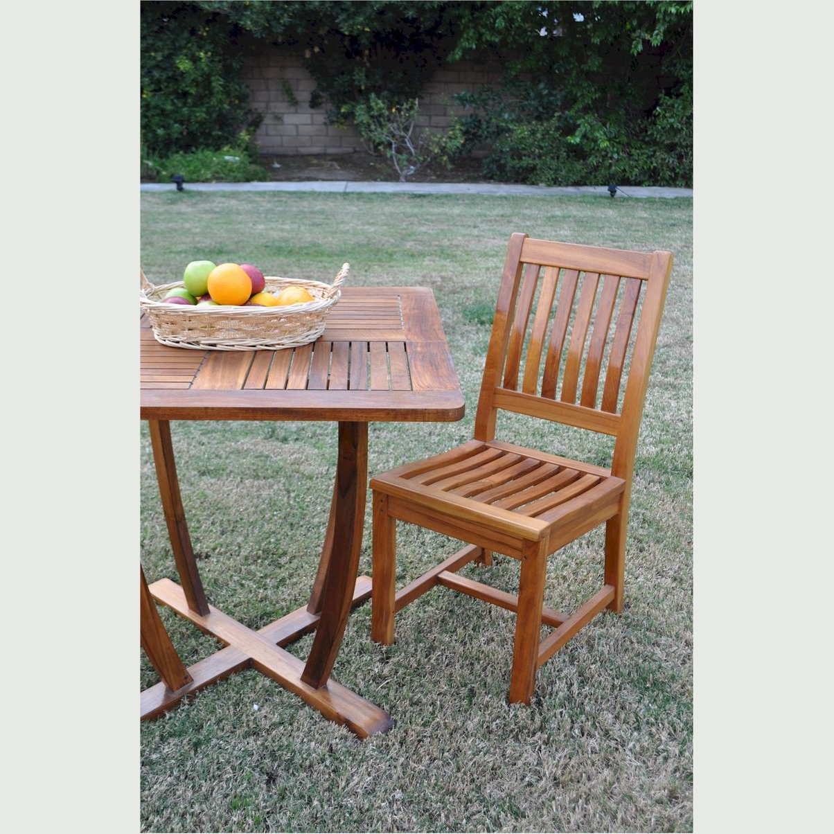 Wooden outdoor table and chair set with a basket of fruit on a grassy area.