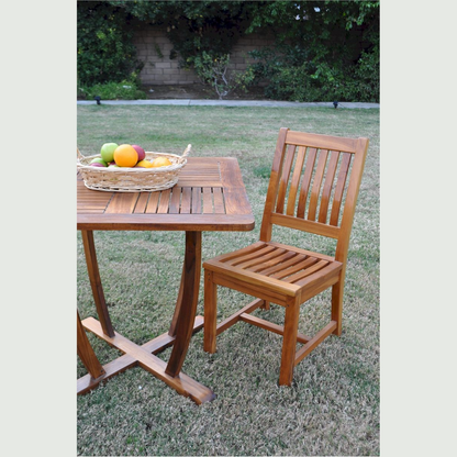 Wooden outdoor table and chair set with a basket of fruit on a grassy area.
