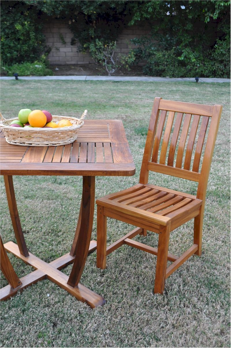 Wooden outdoor table and chair set with a basket of fruit on a grassy area.