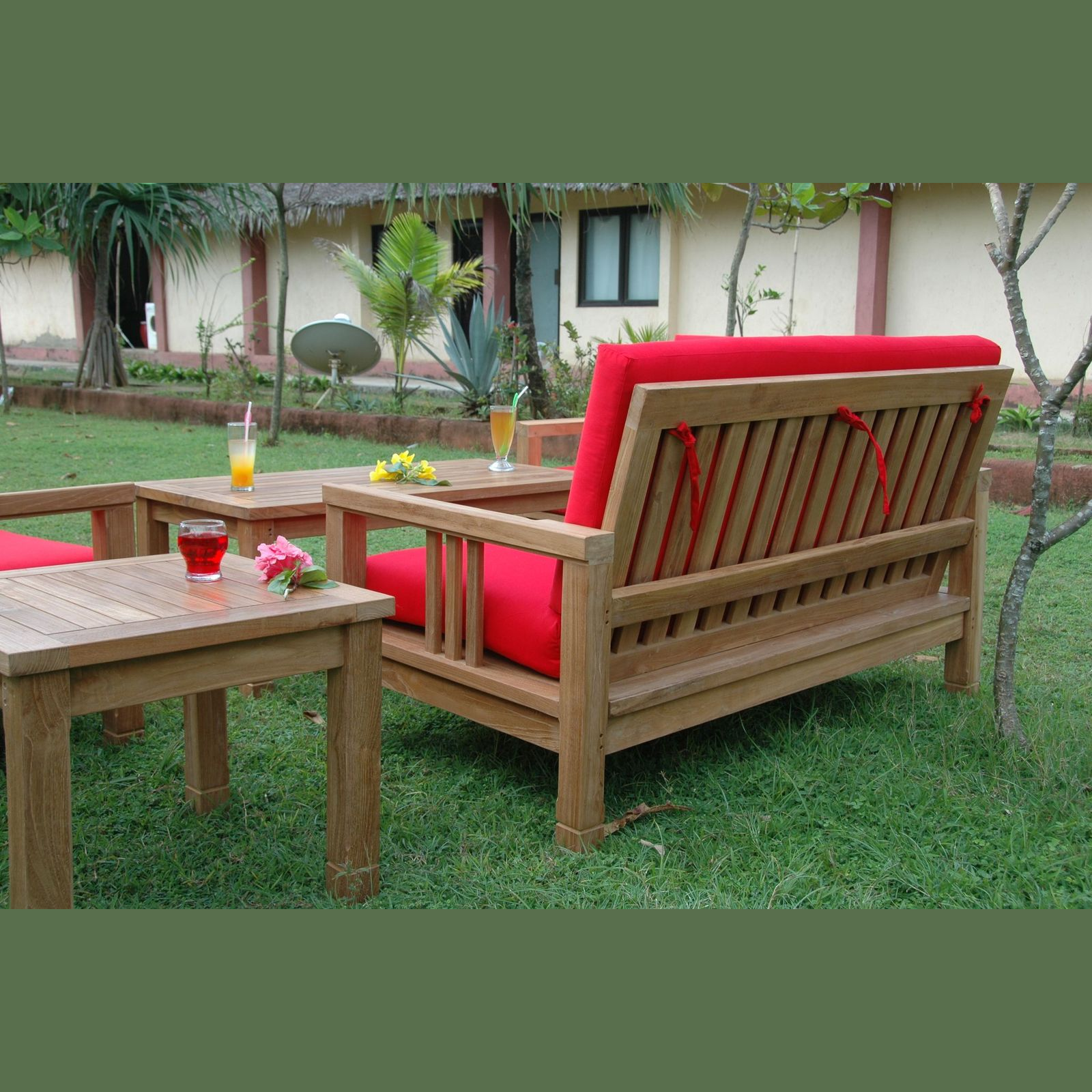 Wooden outdoor furniture set with red cushions on a grassy area.