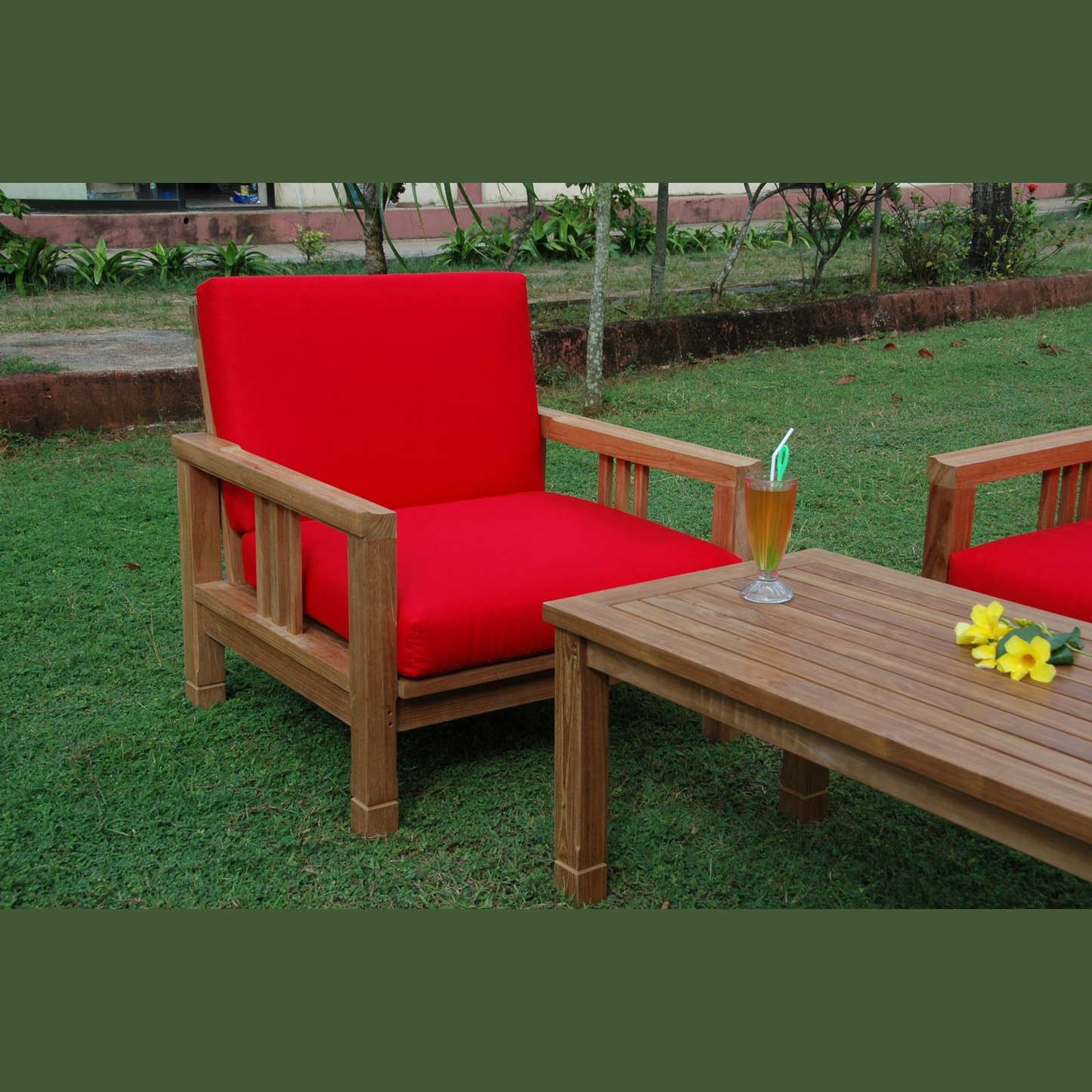 Red cushioned chair and wooden table with a drink on grass