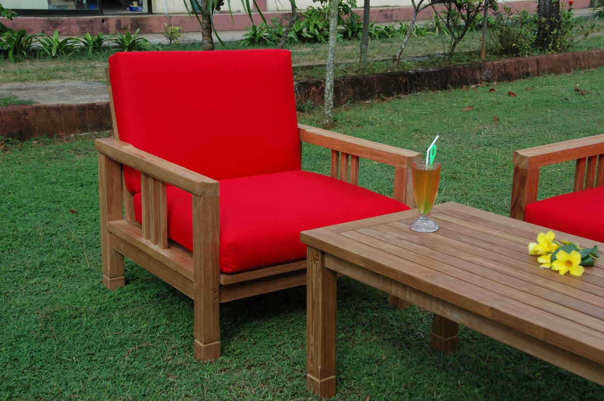Red cushioned chair and wooden table with a drink on grass