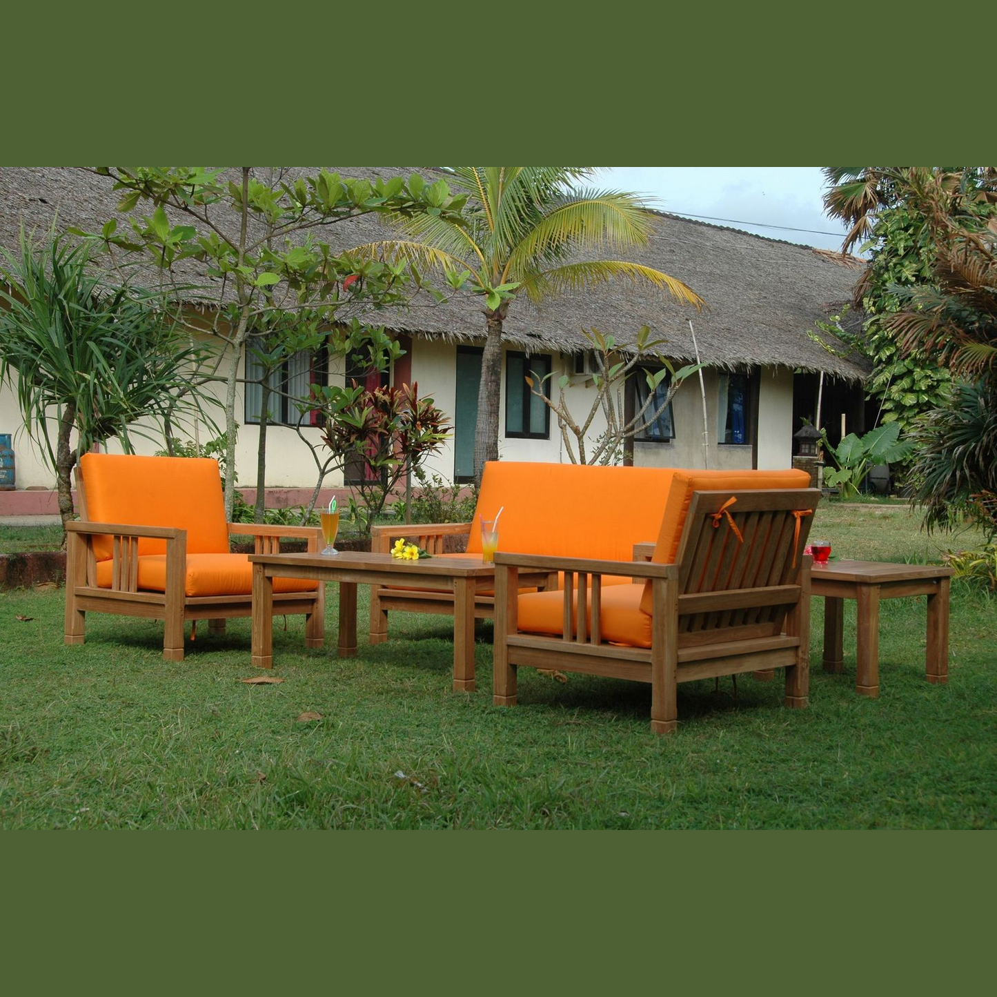 Outdoor furniture set with orange cushions on a grassy area in front of a thatched-roof building.