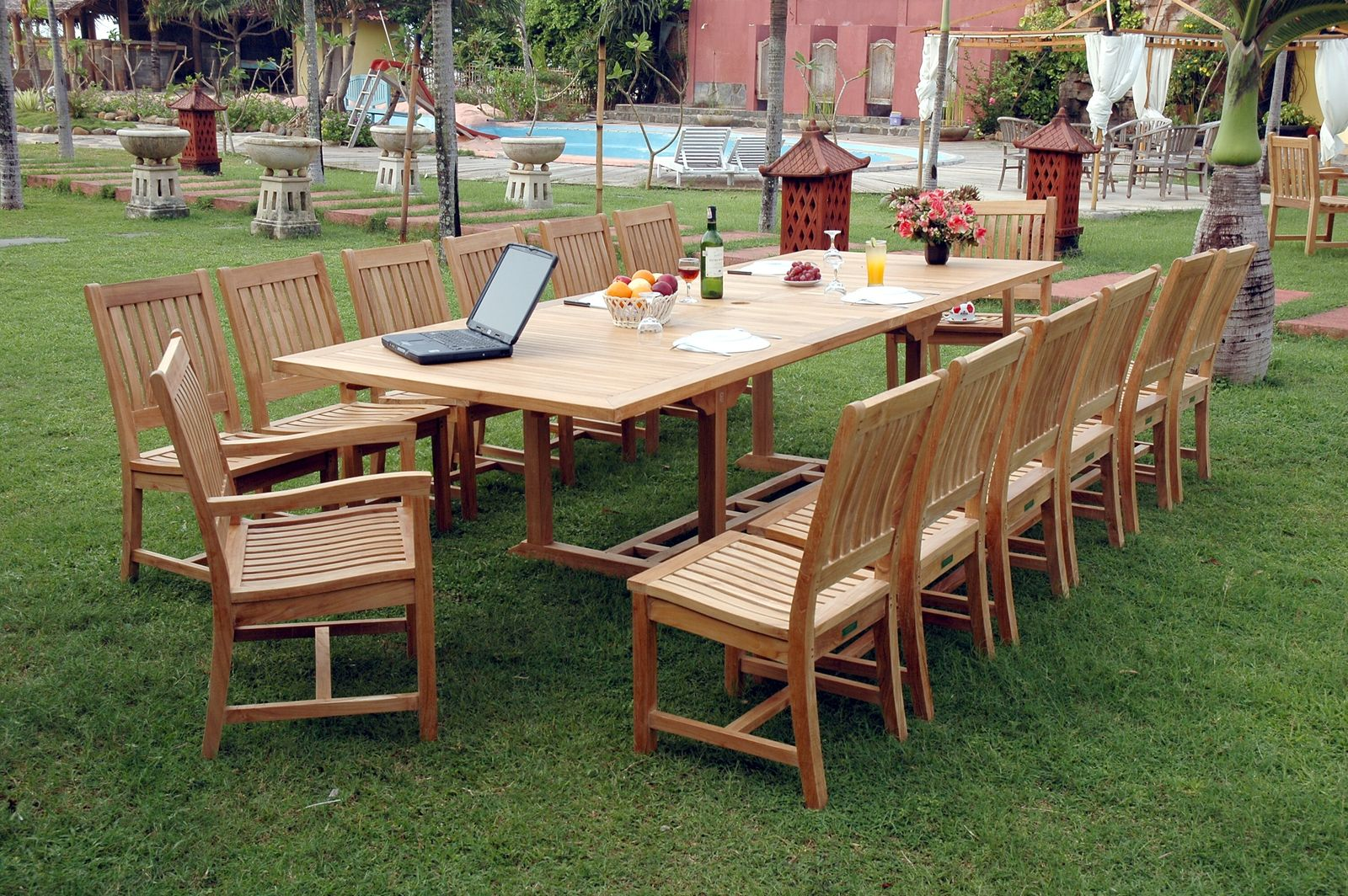 Outdoor wooden dining set with chairs on a grassy area near a pool.