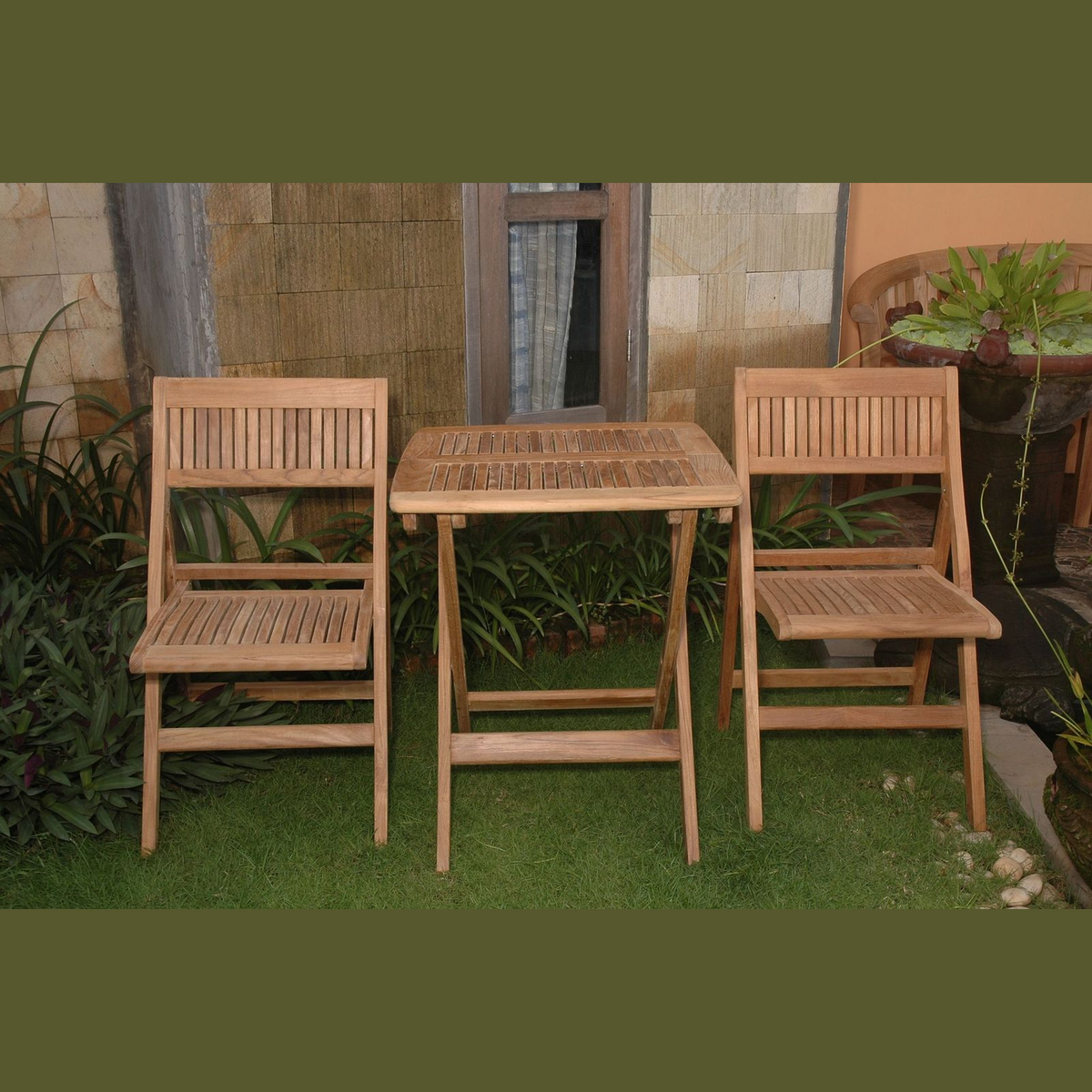 Wooden outdoor table and chairs set on a grassy area with plants and a stone wall in the background.