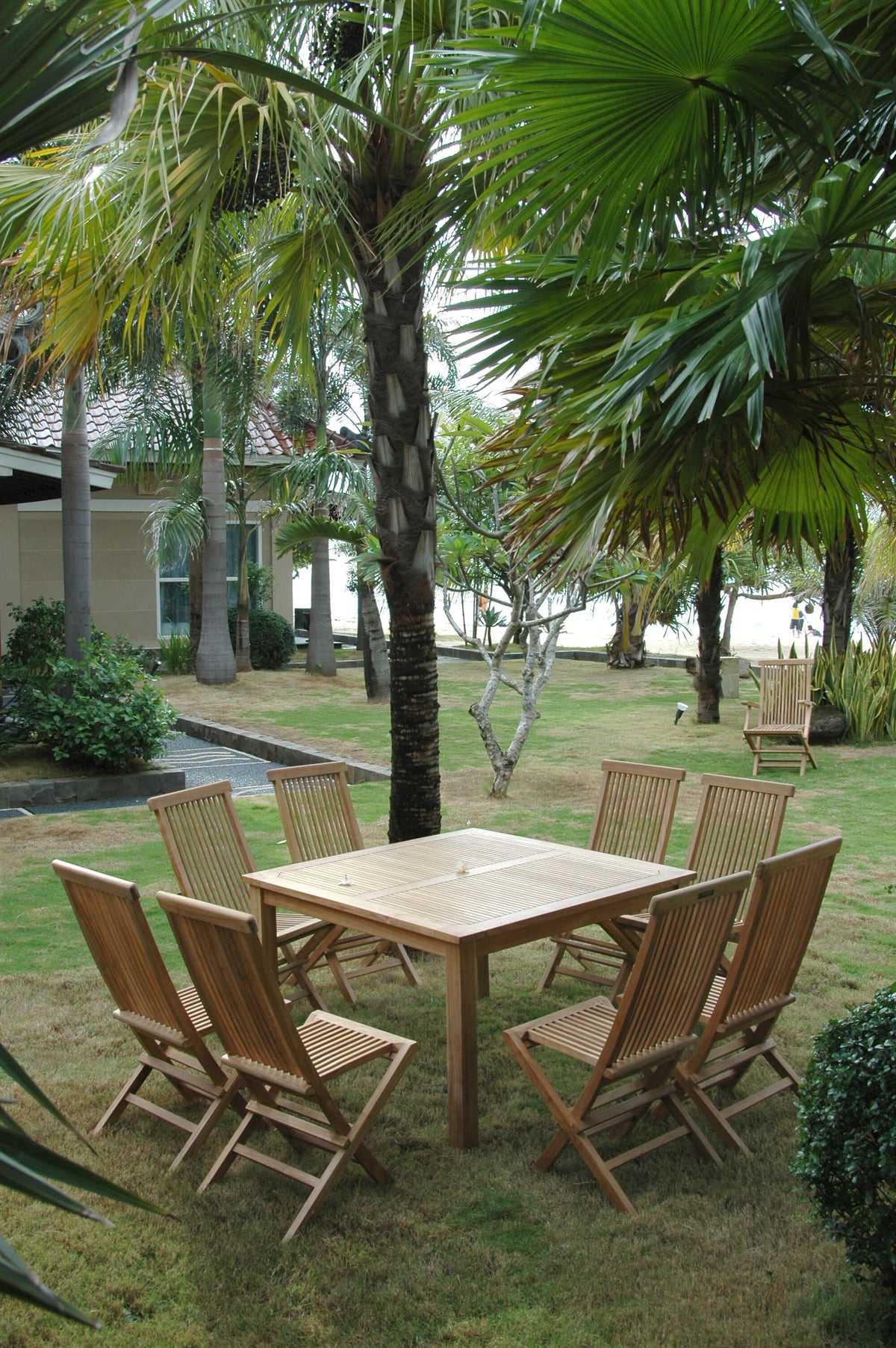 Wooden outdoor dining set with chairs on a grassy area with palm trees.