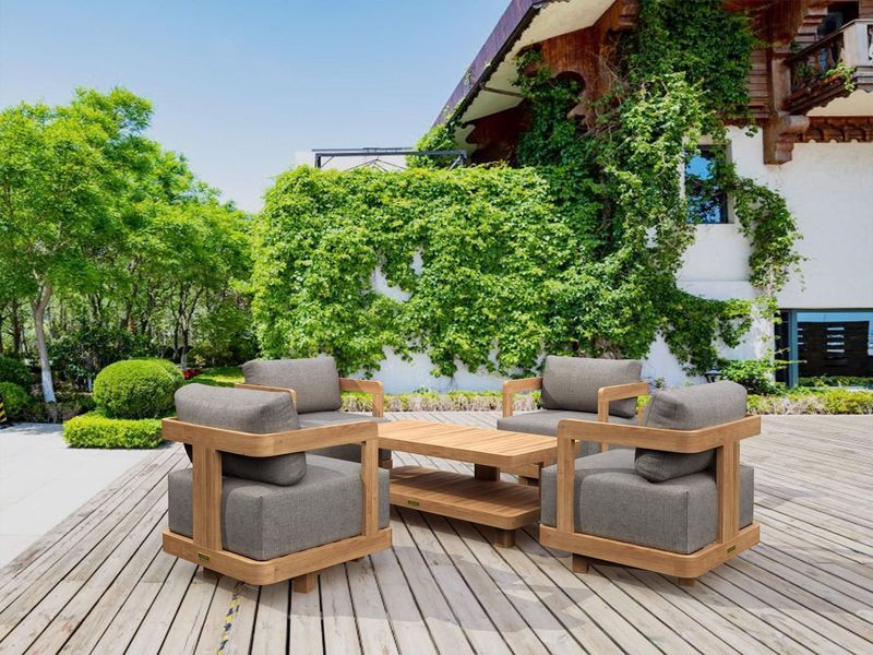 Outdoor patio furniture set on a wooden deck with greenery and a building in the background.