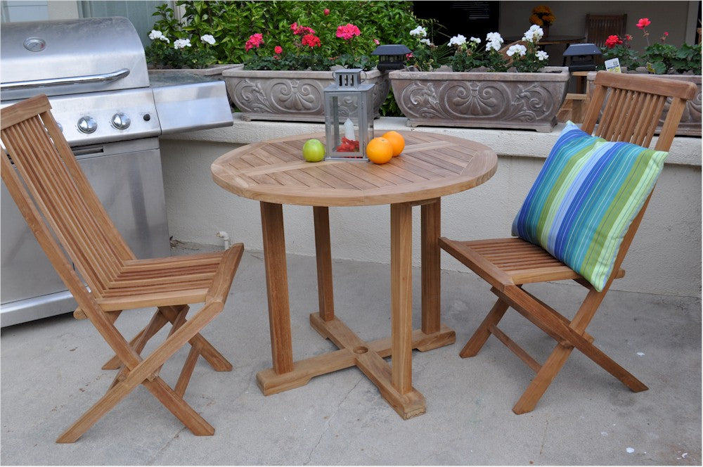 Wooden outdoor table with chairs and a striped pillow, next to a grill with potted plants in the background.