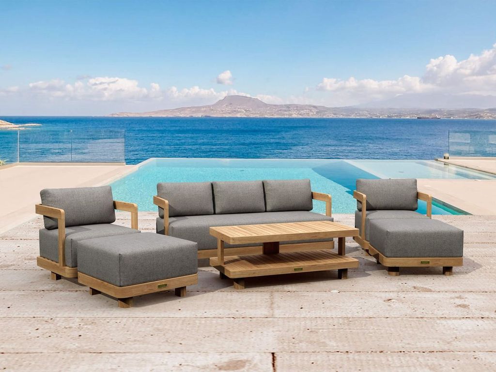 Outdoor patio furniture set with gray cushions and a wooden table by a pool with ocean view.