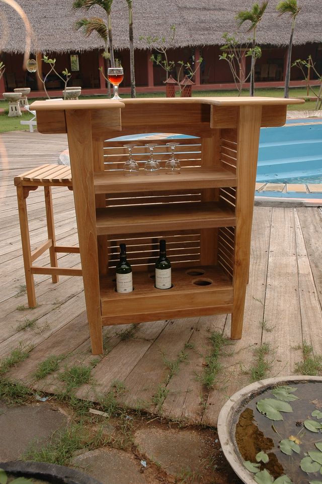 Wooden outdoor bar cart with bottles and glasses on a wooden deck.