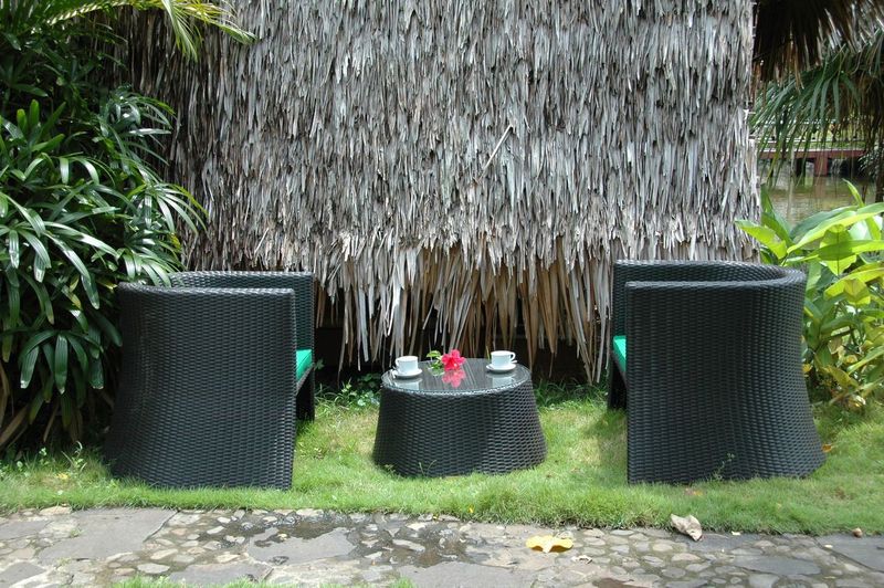 Black outdoor furniture set with a small round table and chairs against a thatched wall.
