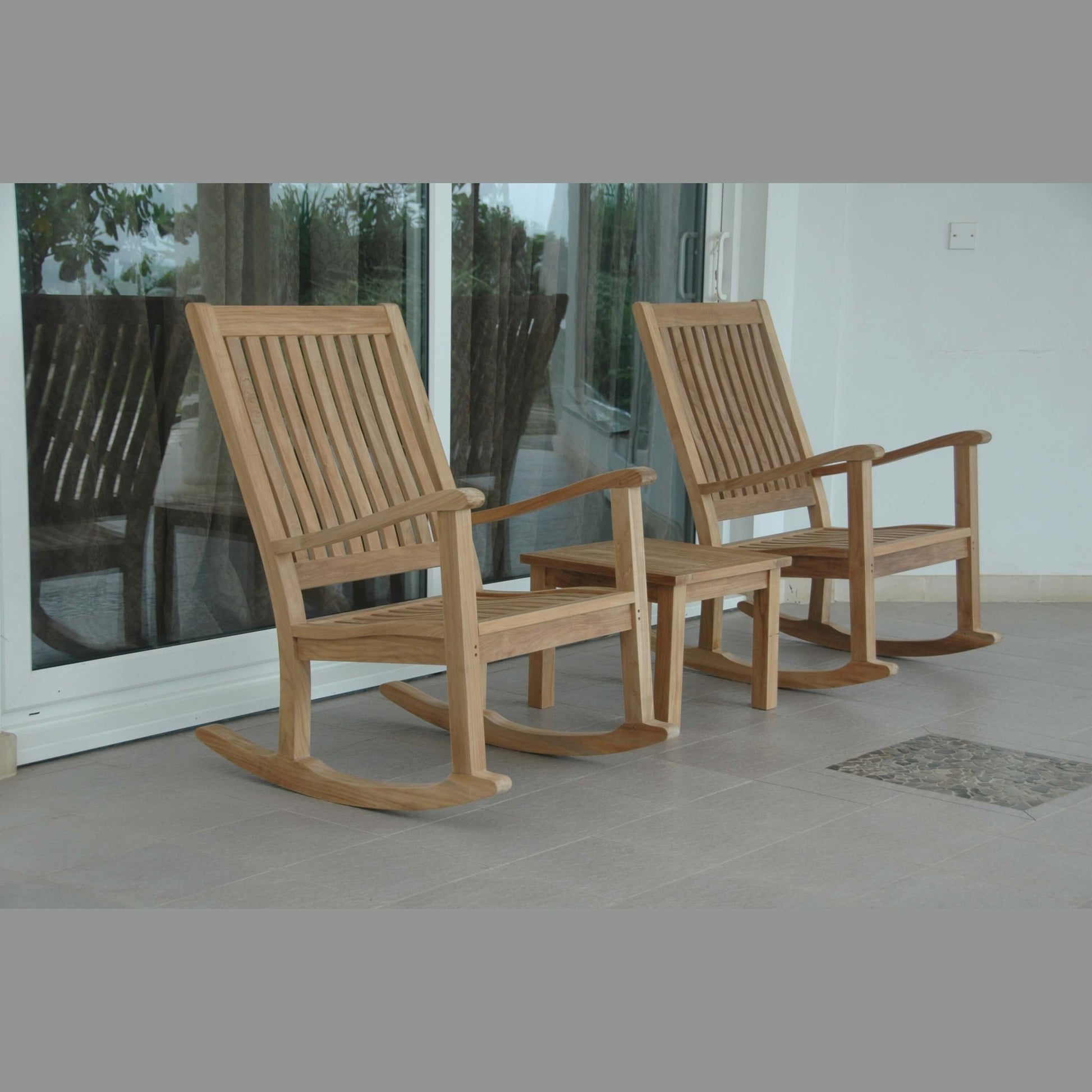 Two wooden rocking chairs on a patio with glass doors in the background.