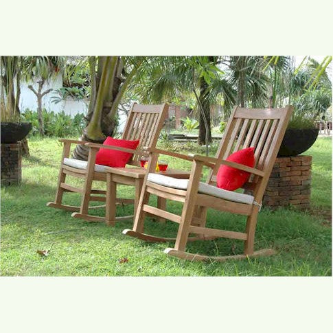 Two wooden rocking chairs with red cushions on a grassy area with trees in the background.