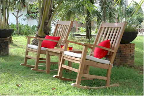 Two wooden rocking chairs with red cushions on a grassy area with trees in the background.
