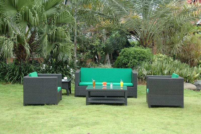 Outdoor furniture set with green cushions on a grassy area with palm trees in the background