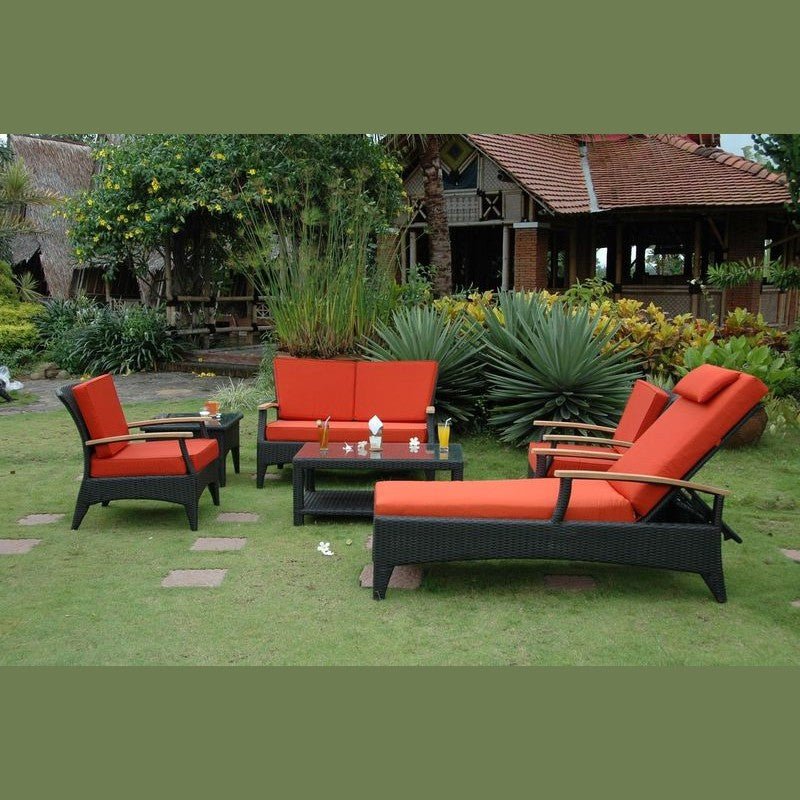 Outdoor furniture set with orange cushions on a grassy area with a building in the background.