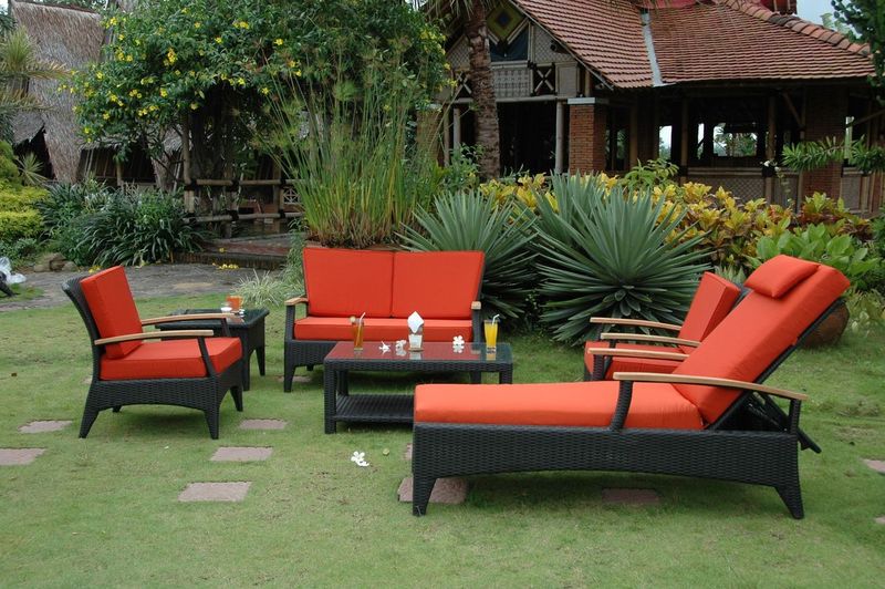 Outdoor furniture set with orange cushions on a grassy area with a building in the background.