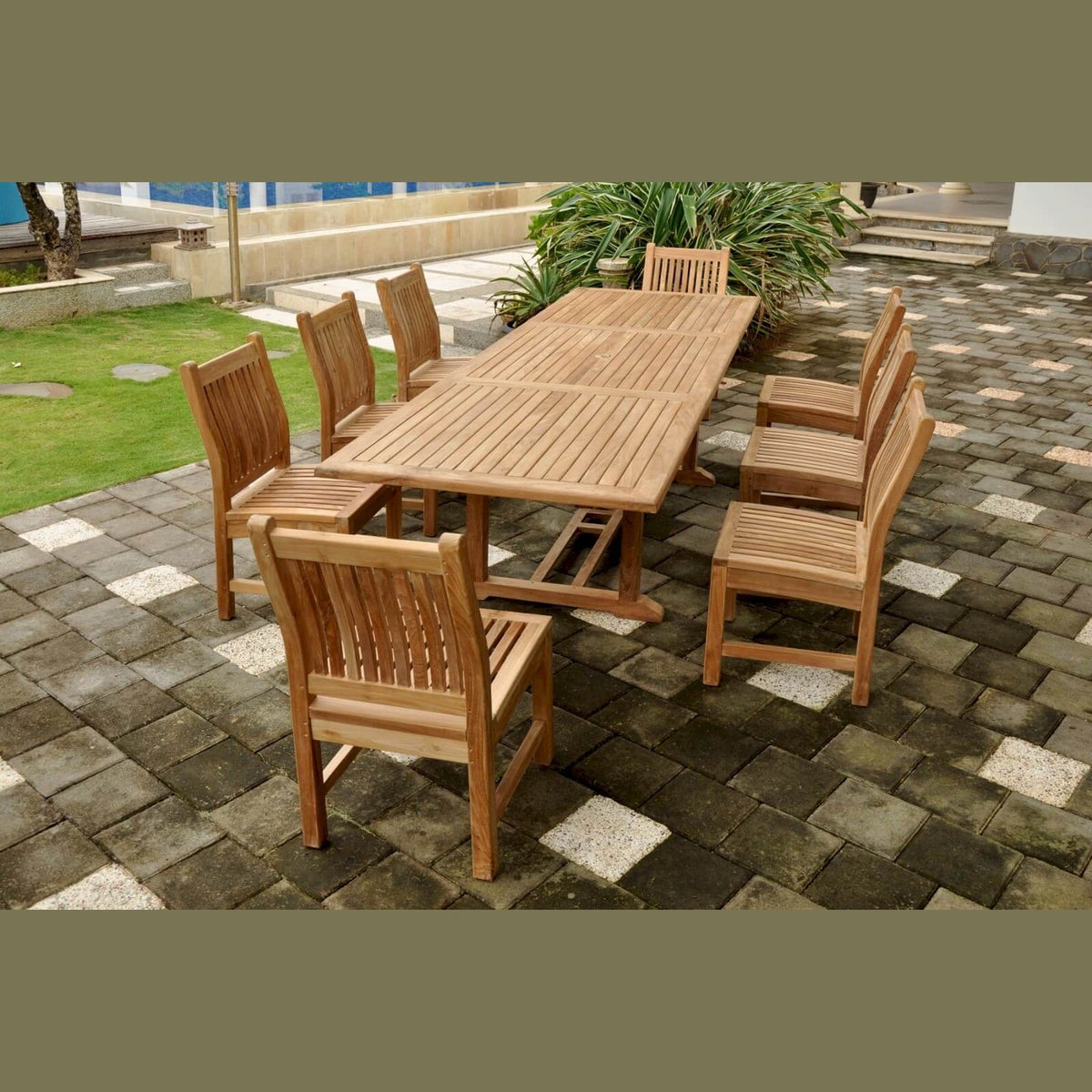 Wooden outdoor dining set on a paved patio with grass and plants in the background.
